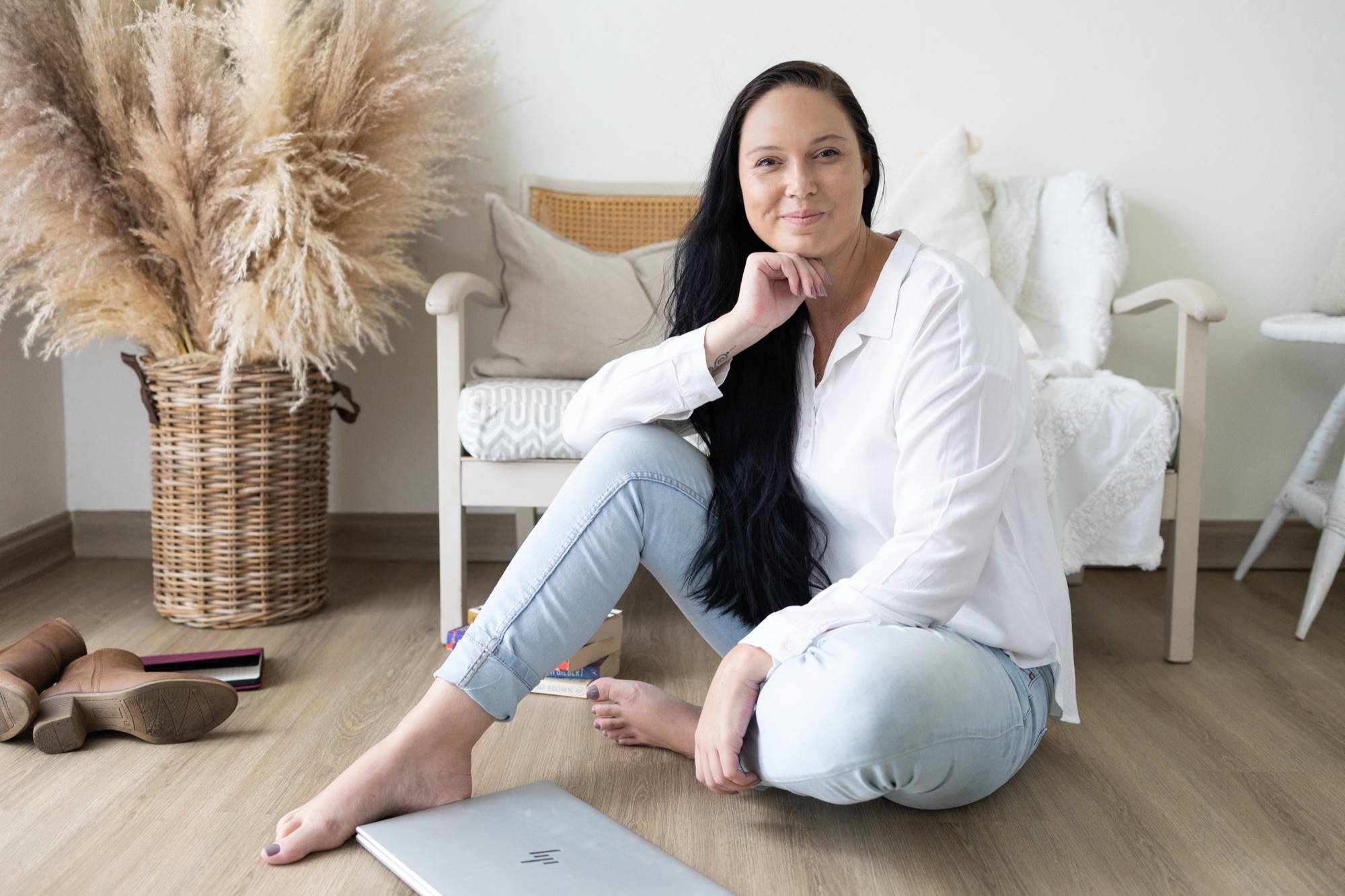 Kirsty Carlson, Founder of Her Collective, seated on the floor of a bright living room beside a laptop and a stack of books