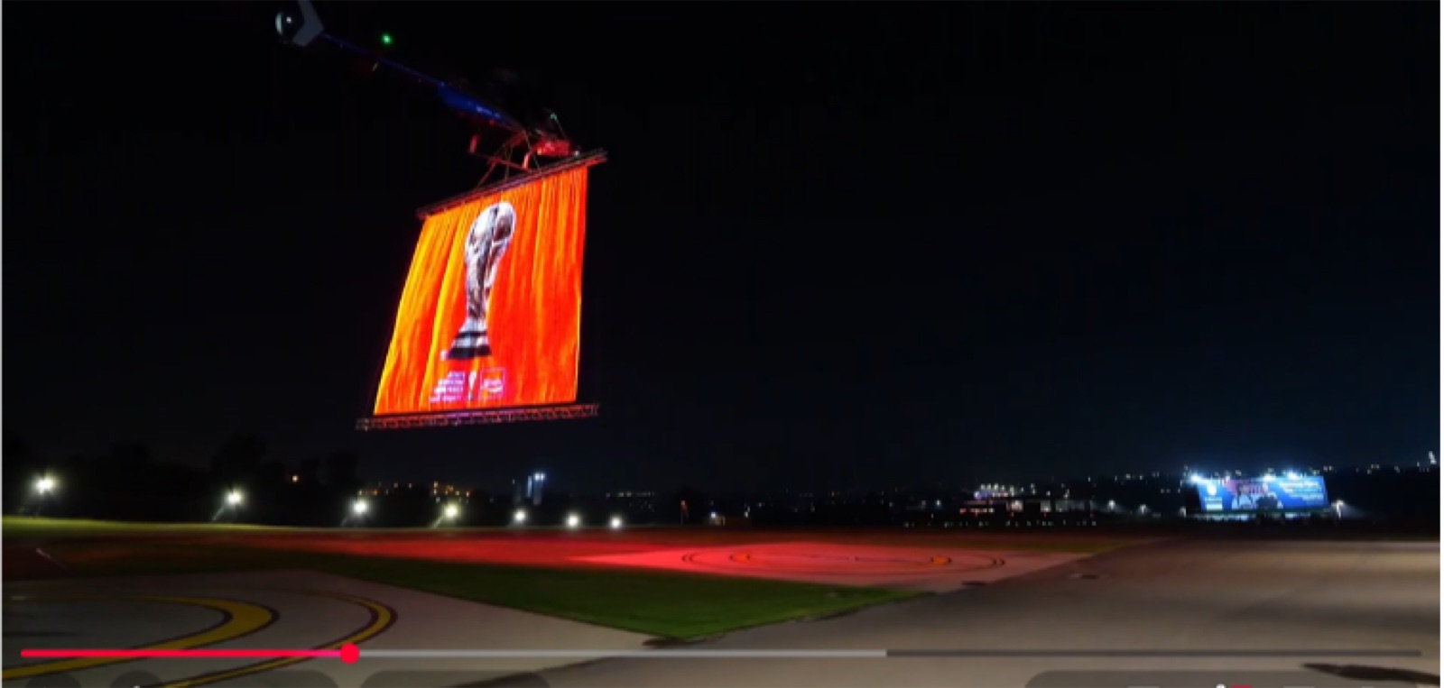 A helicopter carrying a glowing LED mesh screen showing the FIFA World Cup trophy over the N1 at night