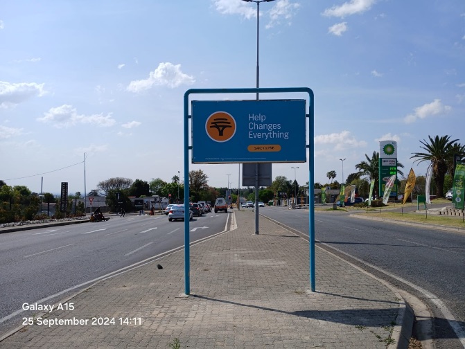 FNB "Help Changes Everything" street pole ad beside a suburban road
