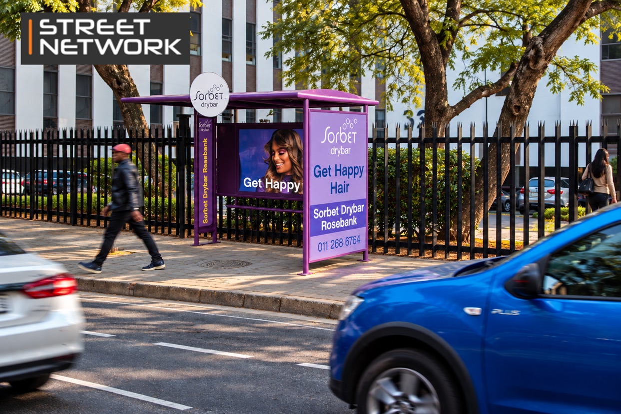 Purple Sorbet Drybar bus shelter ad on a suburban street as a pedestrian walks past